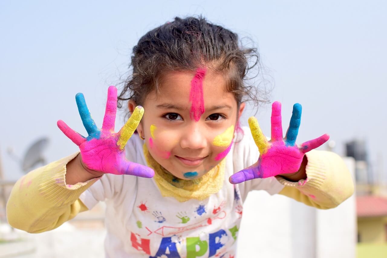 Little girl with bright paint on her face and hands.
